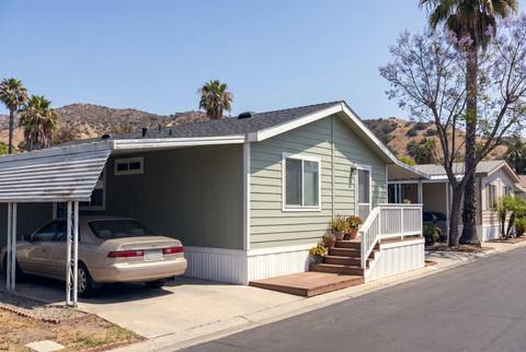 A manufactured home with a carport and a small front deck in a mobile home park.